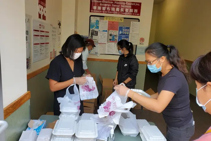 Workers in masks prep boxes of food in room
